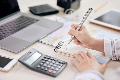 Person writing in a notebook next to a calculator